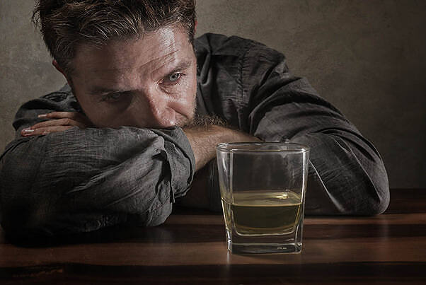 Depressed man staring at a glass of alcohol, illustrating the challenges of giving up drinking