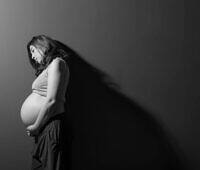 Black and white image of a pregnant woman looking down at her belly with a concerned expression, highlighting the struggle of addiction during pregnancy