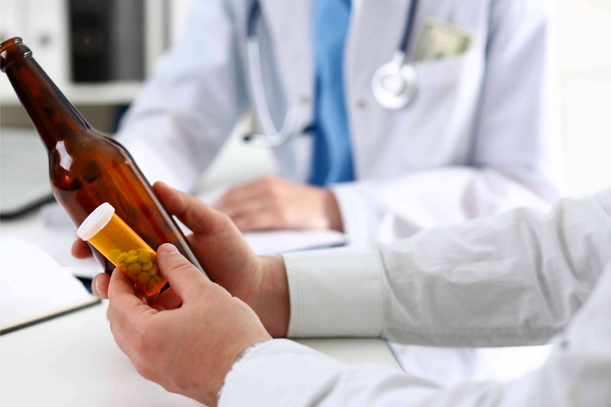 Doctor consulting with a patient holding a beer bottle and pill container, addressing substance dependency issues.