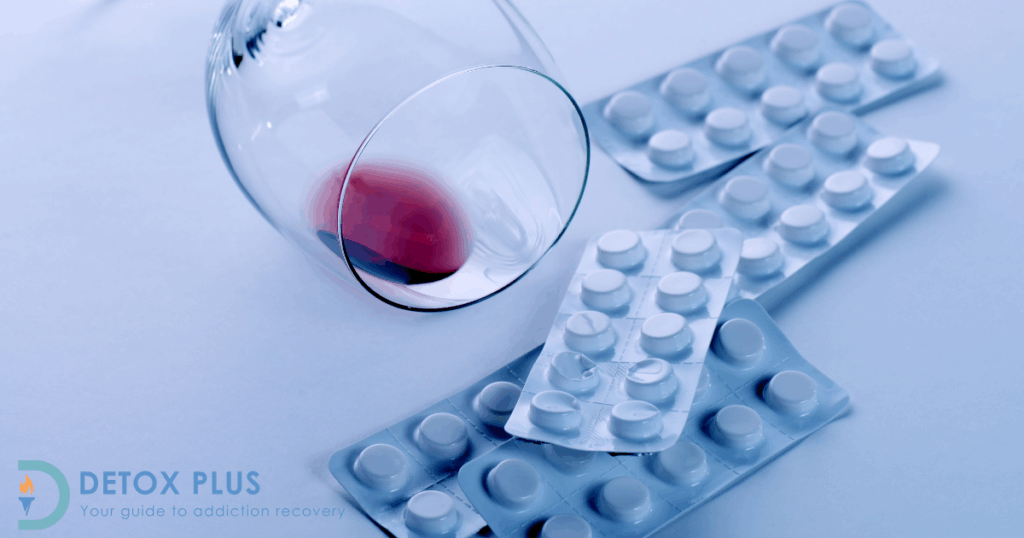 glass of wine fallen over next to packets of antibiotic pills on white background