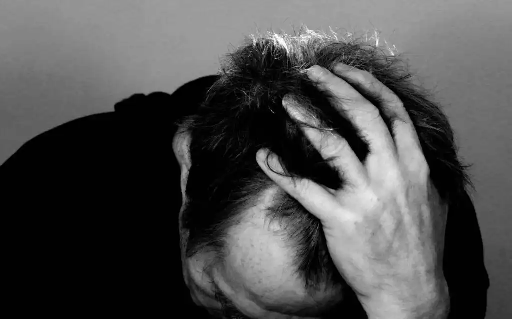 Black and white image of a distressed man with his head bowed and hand gripping his hair, illustrating the emotional struggle of addiction and mental health issues