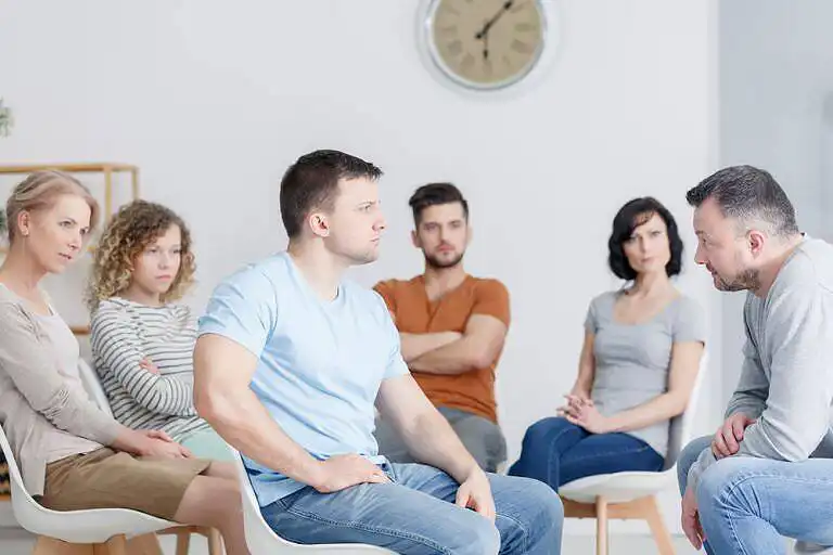 Diverse group of people sitting in a circle during a support group meeting, looking attentive and engaged in a therapy session