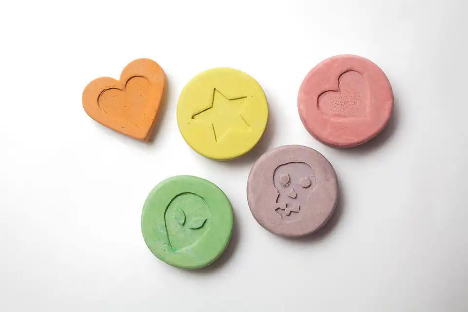 Assorted ecstasy pills in pastel colors featuring heart, star, alien, and skull designs on white background