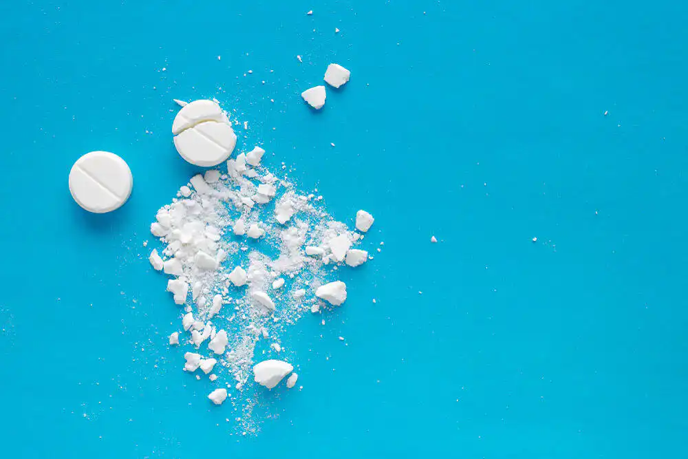 White pharmaceutical pills and powder scattered on bright blue surface, representing opioid medications
