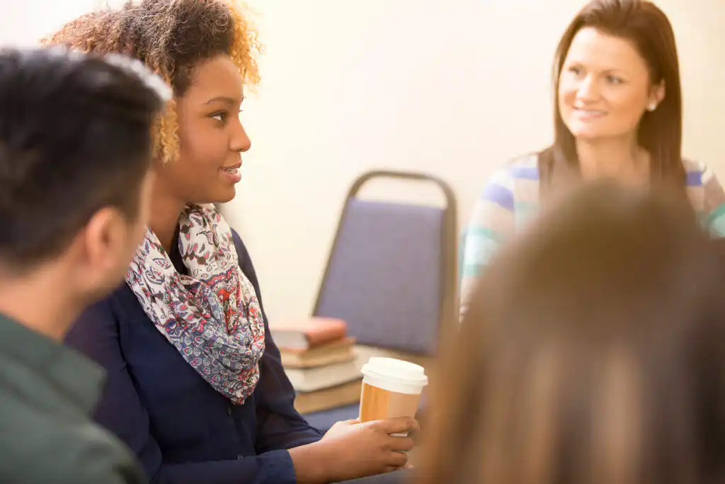 Multi-ethnic group of adults in a supportive counseling session, with a young African American woman speaking to attentive participants.|Stylized illustration of London's Tower Bridge in turquoise on a dark blue background, with text "COCAINE - DETOX LONDON" overlaid, representing cocaine detox services in London