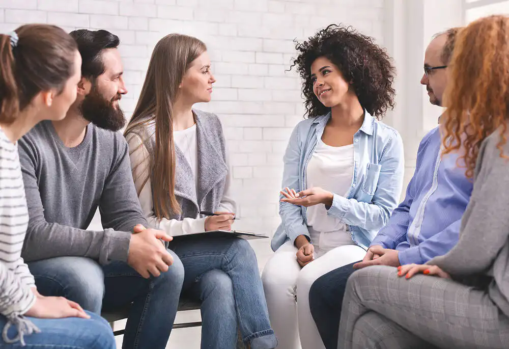 A group therapy session in an alcohol rehab program, featuring participants engaged in discussion|Peaceful Essex beach scene with sandy shore, rocky outcrops, and remnants of a pier, overlooked by hillside houses, symbolizing a calm environment for addiction rehabilitation|Two people holding hands in a supportive gesture, symbolizing care and support during alcohol rehabilitation|Aerial view of Osea Island in Essex, showing a picturesque coastal landscape with green fields, beaches, and buildings, ideal for a peaceful rehabilitation environment