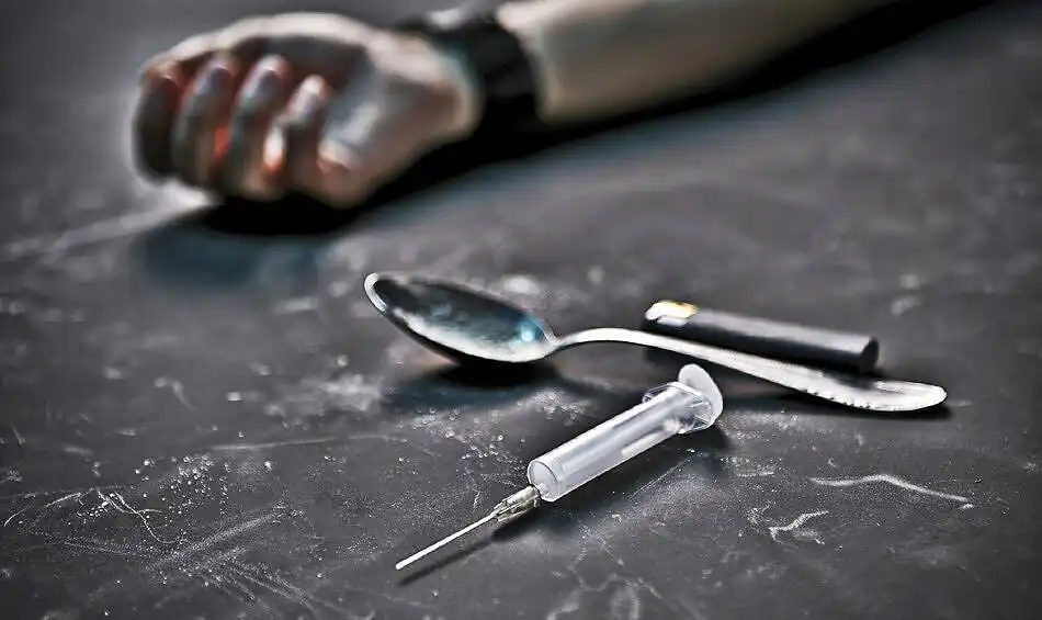 Close-up image of drug paraphernalia including a syringe, spoon, and an outstretched arm, illustrating the harsh reality of heroin addiction