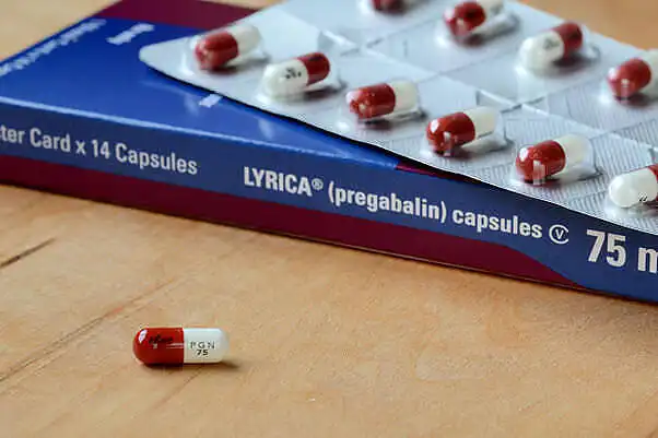 Box of Lyrica (pregabalin) 75mg capsules with red and white pills on blister pack|Young man sitting on a green couch in a kitchen, holding his head in pain while holding a glass of water, displaying signs of a hangover or alcohol withdrawal|Woman experiencing discomfort, holding her head and chest, possibly due to side effects of mixing pregabalin and alcohol