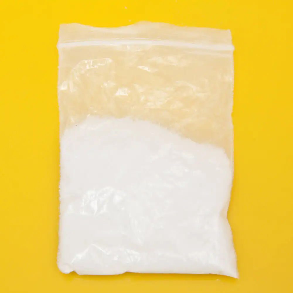 A clear plastic bag containing white powder, commonly associated with mephedrone, on a yellow background, highlighting its appearance for educational purposes in drug awareness.