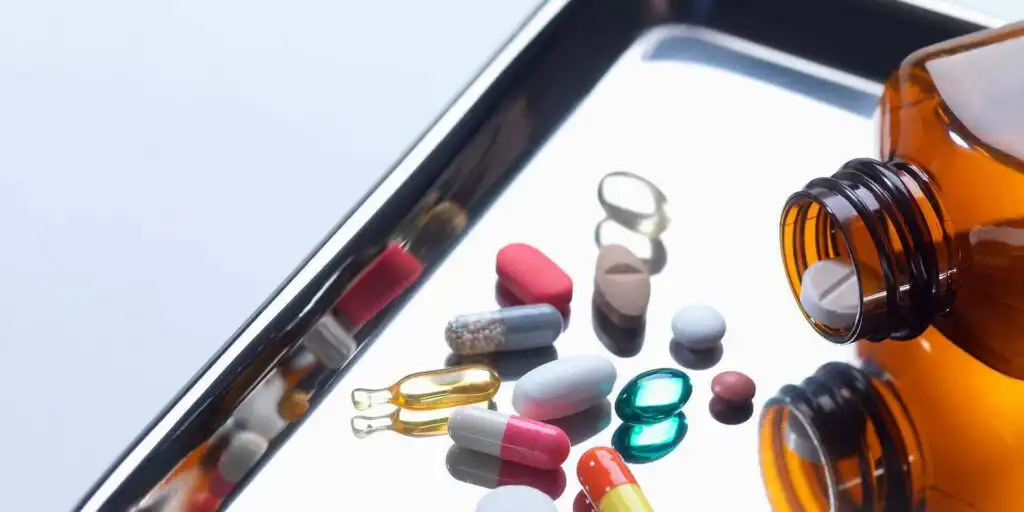 Various prescription pills and capsules scattered on a tablet screen next to an open medication bottle||Illustration of a large red and blue capsule pill labeled 'IQ PILL' with a brain pattern on the blue half, alongside smaller pills, representing cognitive enhancement drugs