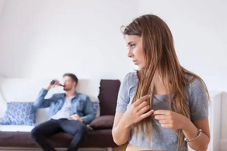 Woman looking distressed while man drinks alcohol in background, illustrating relationship problems due to substance abuse|Conceptual image depicting denial in functioning alcoholics: three people with heads buried in sand on a beach, with 'DENIAL' text overhead