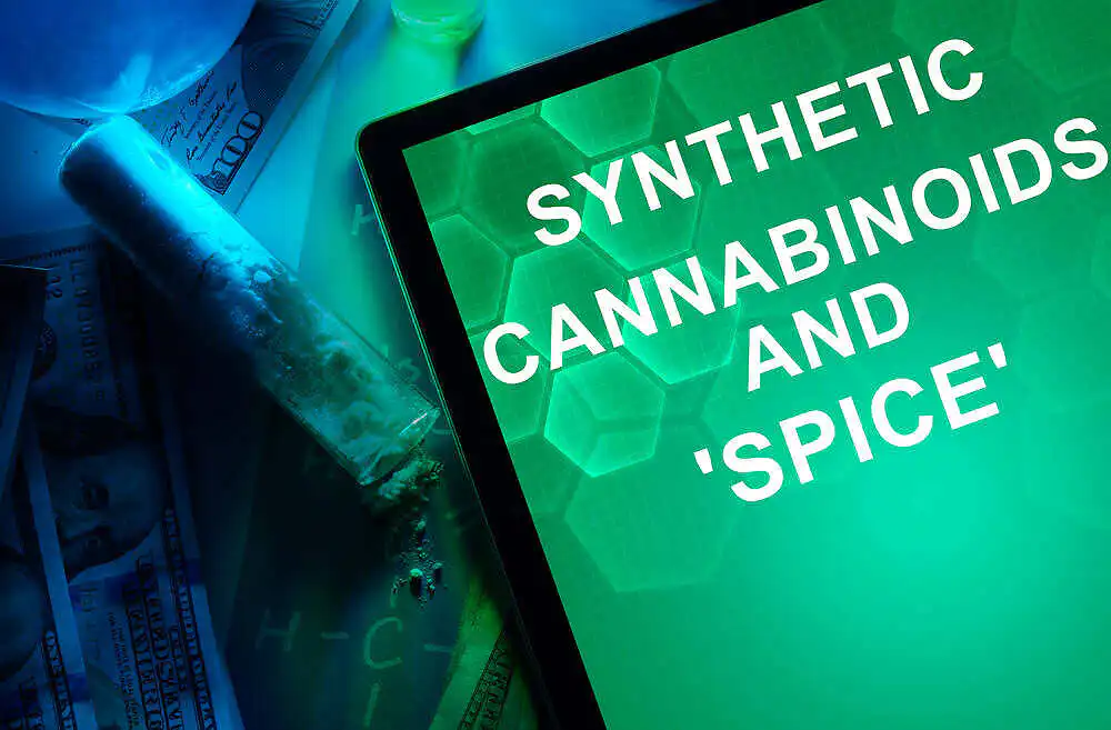 Tablet screen displaying "Synthetic Cannabinoids and 'Spice'" text with drug paraphernalia and money in the background|Black and white image of a person's silhouette exhaling a cloud of smoke, illustrating the use of Spice drug|Packet of synthetic cannabis labeled "Spice Diamond" with eye logo, next to pile of dried herbal material, illustrating the appearance of dangerous synthetic drugs