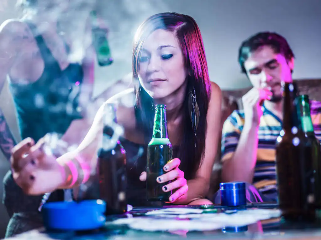 Young woman drinking alcohol and smoking at a party, surrounded by beer bottles and cigarettes, illustrating teenage substance abuse