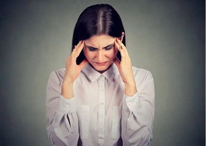 Woman in white shirt holding her head, appearing to have a headache or experiencing stress|Female doctor consulting with distressed patient about mogadon addiction in medical office